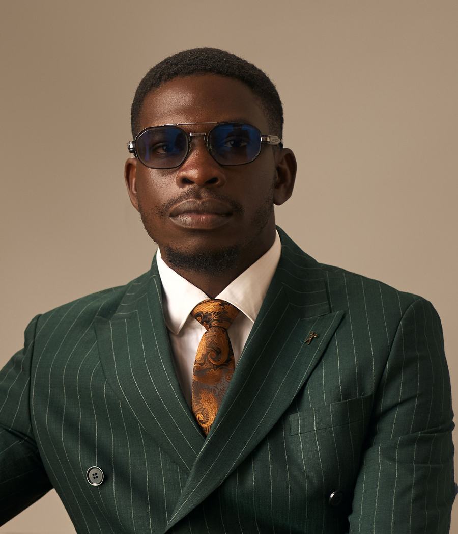 Seun Mosaku in a green pinstripe double-breasted suit and blue-tinted glasses